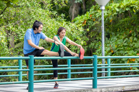 Outdoors on the bridge, an attractive young fitness couple stretching, a sporty guy and woman exercising together.の写真素材
