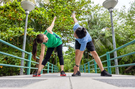 Outdoors on the bridge, an attractive young fitness couple stretching, a sporty guy and woman exercising together.の写真素材