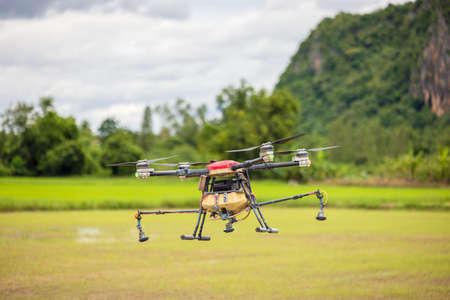 Agriculture drones fly over rice fields sprinkling fertilizer, High-resolution photographs of industrial drones spraying chemicals on rice paddies and fieldsの写真素材