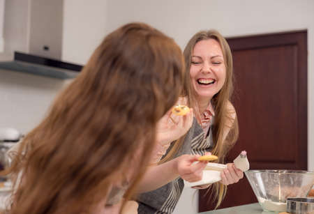Expectant mother and daughter decorating cupcakes on a kitchen table, having a good time together while eating freshly baked pastriesの写真素材