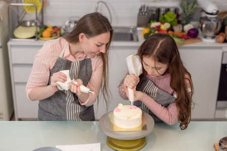 Expectant mother and daughter decorating cupcakes on a kitchen table, having a good time together while eating freshly baked pastriesの写真素材