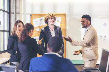 Multi-ethnic business team various office workers conversing and smiling while holding a meeting with colleagues in a modern office, senior businessman making a backdrop presentationの写真素材