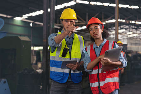 A portrait of a manufacturing worker in discussion with an industrial man and woman engineer holding...