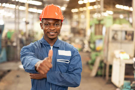 Portrait of a black factory worker in a hardhat staring at the photo while standing in a workshop,...