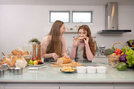 Mom and her younger kids daughter in a modern kitchen area celebrating joyous learning, baking, cake...