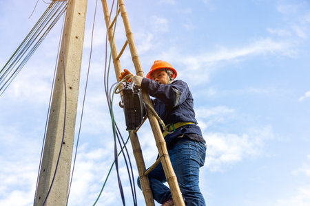 A telecoms worker is shown working from a utility pole ladder while wearing high visibility personal...