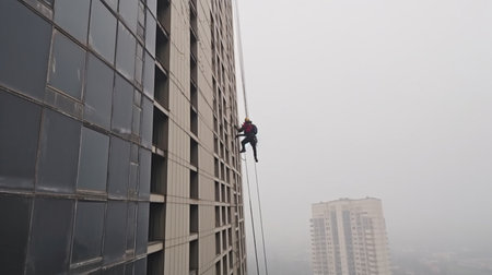 Industrial mountaineer worker washing outside faÃ§ade glazing, hanging over building, Generative AIの素材