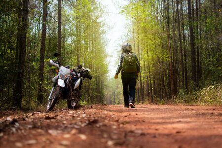 A young man traveling alone on forest with luggage and motorcycle road rock dust torch light yellow.の写真素材