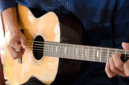 A young man playing acoustic guitar happy and relaxed in the daytime focal point on the details.