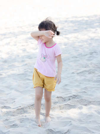 Positive charming 4 years old cute baby Asian girl, little preschooler child playing on sand beach on beautiful sunny day in summer time. Selective focus.の写真素材