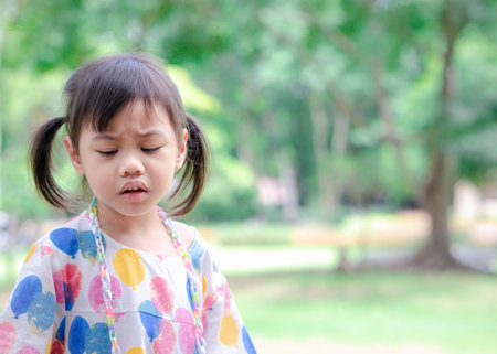 Headshot of sad 4 years old cute baby Asian girl, little toddler child with adorable pigtails hair making frustrated face, looking down with copy space background.の写真素材