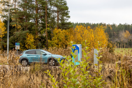 Electric car is charging at a charging station in a natural surrounding with autumn colors in Swedenの写真素材