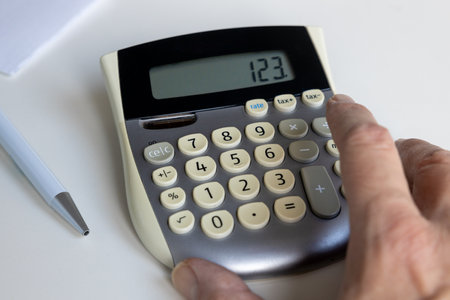Close up of a calculator with hand and pen and paperの写真素材