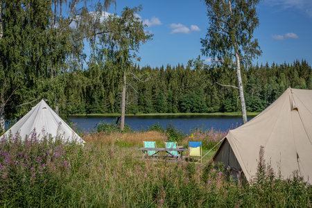 Panoramic view of a Swedish lake with two tents and three camping chairsの写真素材