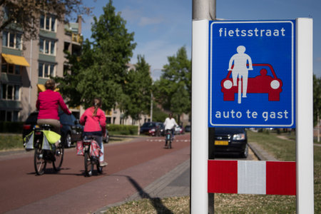 Mother and child cycle next to each other on a bicycle street where cars are guests in the city of Deventerの写真素材