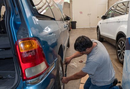 man changing a wheel from a blue truck using only hand toolsの写真素材