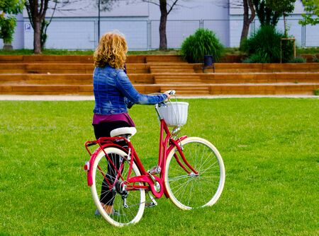 Curly-haired blonde woman walking in the park on a red bicycleの写真素材