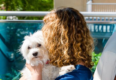 Blonde curly-haired woman on the balcony of home hugging her puppy