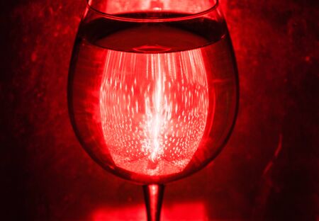 Glass of wine on red background. Light reflectionsの写真素材