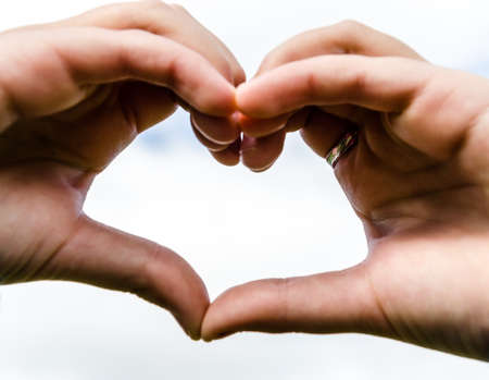 Close-up of heart-shaped hands against the sky