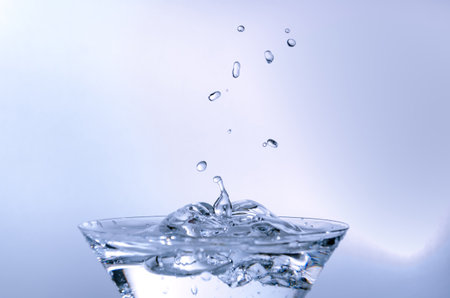 Close-up of water drop falling into a glass on white backgroundの写真素材