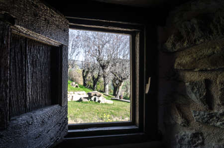 Interior view from the window of a rustic house towards a beautiful garden with trees