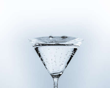 Close-up of water drop falling into a glass on white backgroundの写真素材