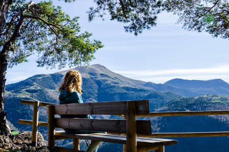 Blond woman with curly hair, sitting on the mountain, looking at the fantastic views of the Ribes Valley, in the Ripolles region, Gironaの写真素材