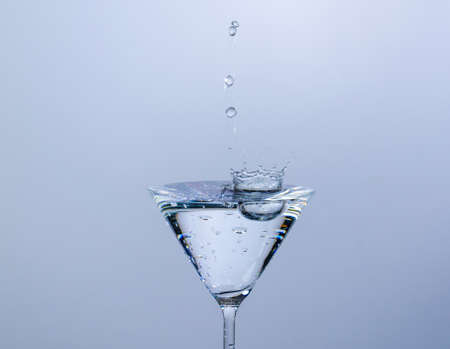 Close-up of water drop falling into a glass on white backgroundの写真素材
