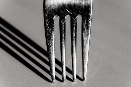Closeup of a fork vertically on a white surface, with a harsh shadowの写真素材