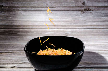 Close-up of cooked polyphosphate noodles falling into a ceramic bowl on a wooden tableの写真素材