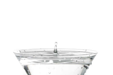 Close-up of water drop falling into a glass on white backgroundの写真素材