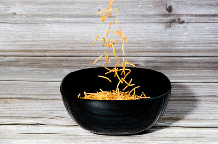 Close-up of cooked polyphosphate noodles falling into a ceramic bowl on a wooden tableの写真素材
