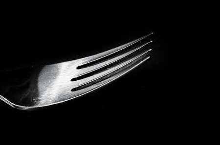 Close-up of a fork horizontally on a black surface, shadow reflectionの写真素材
