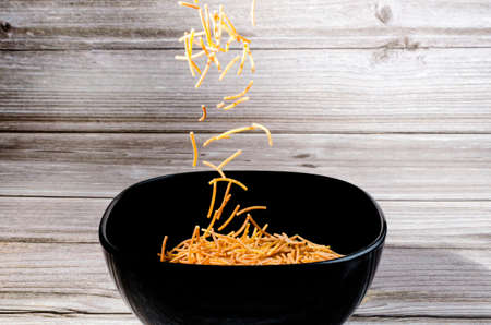 Close-up of cooked polyphosphate noodles falling into a ceramic bowl on a wooden tableの写真素材