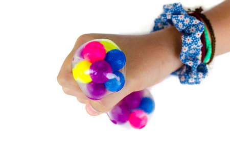 Hand of a girl squeezing a colorful stress ball on white background. Improved motor skills