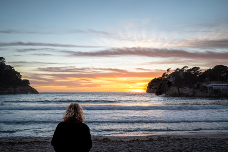 Lonely blonde woman watching the sunset in winter at Galdana beach in Menorca