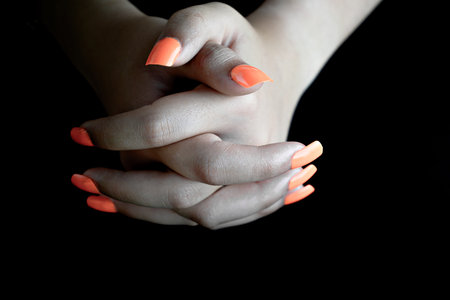 Selective focus of intertwined female hands with orange false nails, on black background. nails manicureの写真素材