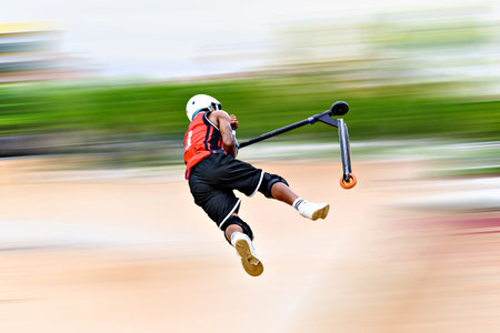 Young man practicing Scootering (Freestyle Scootering) in the park of Igualada, Barcelona, Spain....