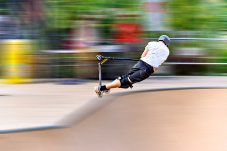 Young man practicing Scootering (Freestyle Scootering) in the new SkatePark in the central park of...