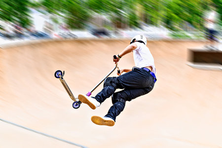 Young man practicing Scootering (Freestyle Scootering) in the new SkatePark in the central park of Igualada, Barcelona, Spain. blurred backgroundの写真素材