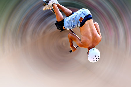 Young man practicing Scootering (Freestyle Scootering) in the new SkatePark in the central park of Igualada, Barcelona, Spain. blurred spiral backgroundの写真素材