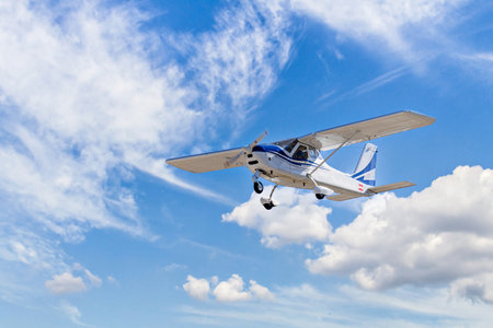 Single engine ultralight plane flying in the blue sky with white cloudsの写真素材