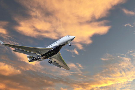 Private business plane flying under orange sunset skyの写真素材