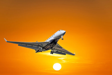 Private business plane flying under orange sunset skyの写真素材