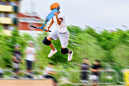 Young man practicing Scootering (Freestyle Scootering) in the new SkatePark in the central park of...