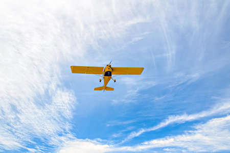 Yellow single-engine ultralight airplane flying in the blue sky with white clouds