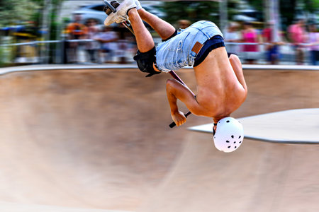 Young man practicing Scootering (Freestyle Scootering) in the new SkatePark in the central park of...