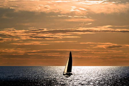 View of a sailing boat at sunset passing in front of the lighthouse, Ciutadella, Menorca, Balearic Islands, Spainの写真素材