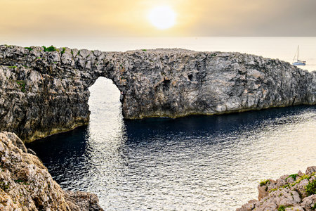 Spectacular sunset at Pont d'en Gil â Cala Corbetar in Ciutadella, Menorca, Balearic Islands. Peculiar natural formation in the form of an archの写真素材